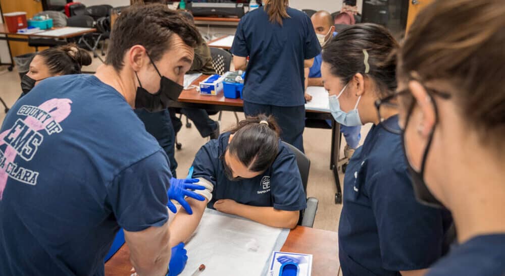 An instructor at Bama Institute teaches Phlebotomy students the how to palpate the arm to find a vein.